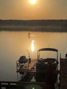 image of Jane Atkinson paddle boarding on the lake at her cottage at sunrise with her dock and boat in the foreground to show wanting what you want